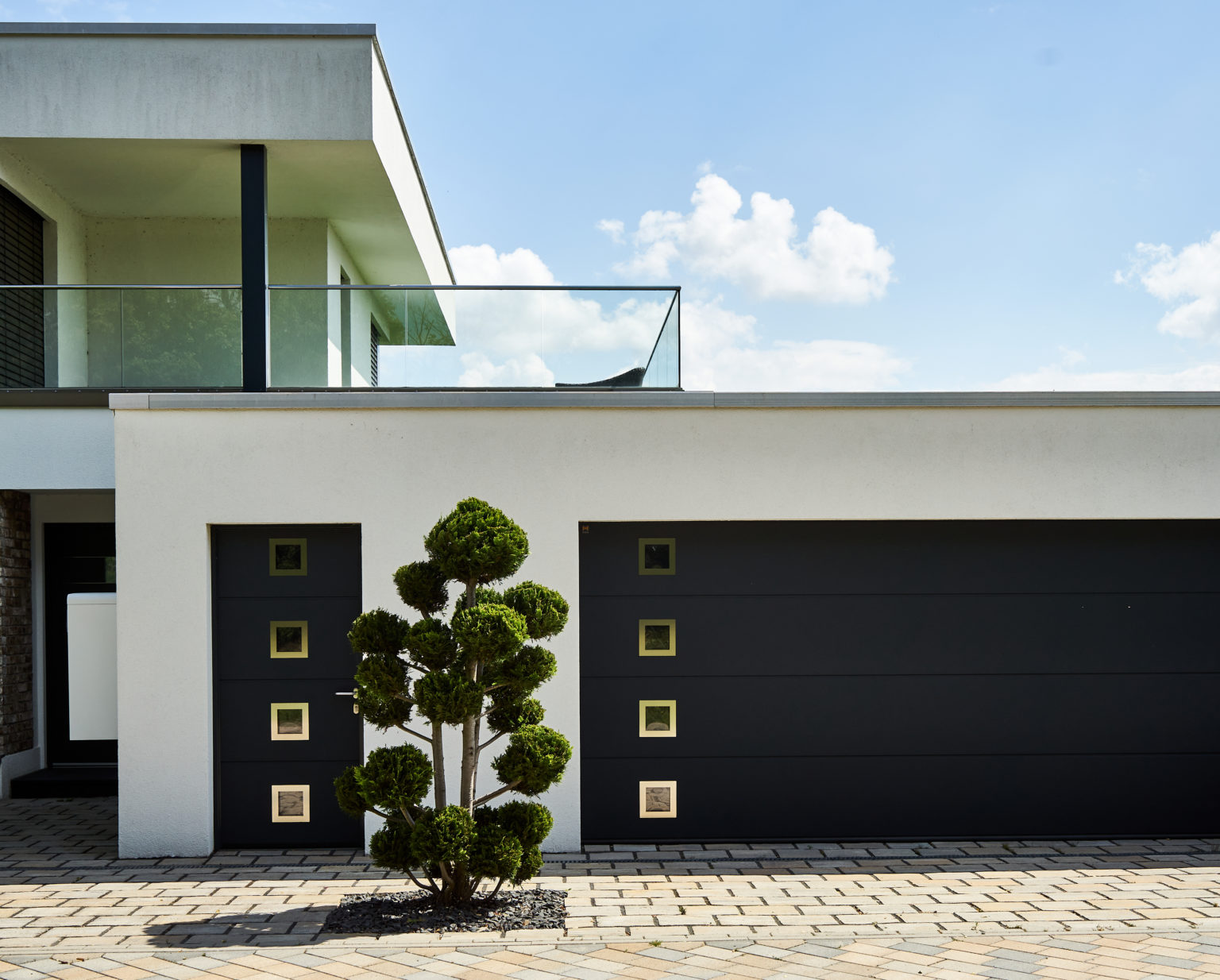 Entrance and garage of a house in minimalist design, with an unnaturally trimmed tree, view from public ground